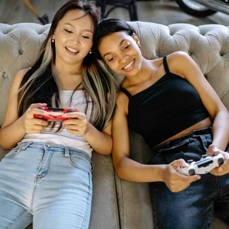 Two young women enjoy gaming together on a cozy sofa, showcasing leisure and camaraderie.